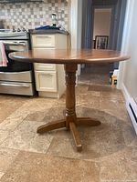 Full view of round dining table with leaves extended, showing wooden finish and pedestal base