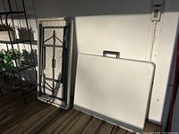 Two plastic folding tables in folded position showing textured underside and metal foldable legs.