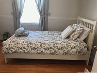Full view of assembled white IKEA double bed with mattress, floral duvet and pillows