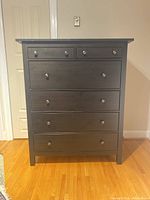 Front view of the dark wood Ikea dresser showing five drawers with metal round knobs.