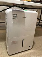 Front-left perspective of white Insignia dehumidifier with collection tank and label attached.