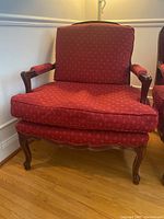 Front view of the lounge chair showing red patterned fabric upholstery, cushioned seat and back, and wooden carved legs and armrests.