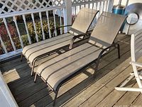 Photo of two tan plastic mesh patio loungers with metal frames on an outdoor wooden deck, showing the loungers side by side and the adjustable backrests.