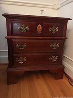 Front view of wooden side table with three drawers, brass drawer pulls, and carved floral detail in center drawer.