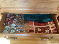 Photo showing drawer contents with placemats, napkin rings, spoon rests, and silver plated spoons.