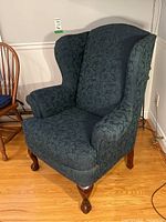 Front angled view showing upholstery and wooden legs of wingback chair.