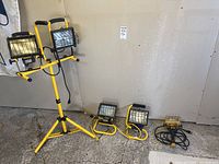 Front view showing the dual-head work light on tripod stand and four additional portable work lights in yellow with black guards.