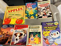 Image of eight assorted Scholastic children's books arranged on a chair showing varied titles and covers.