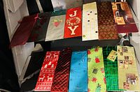 Photo showing 12 assorted wine bottle gift bags in various holiday and general themes with different colors and patterns including grapes, holiday motifs, quilted texture, and wine illustrations.