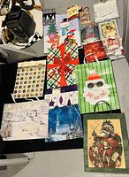 Image shows 13 assorted Christmas-themed gift bags in varying sizes and designs laid out on floor.