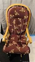 Front view of wooden glider rocker chair, showing padded floral upholstered seat and backrest, light wooden arms and curved frame.