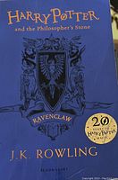 Photo of the front cover of a blue hardcover book, showing Ravenclaw crest and author's name J.K. Rowling, with a 20 years Harry Potter Magic sticker