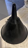 Single photo showing a large black plastic funnel with a wide opening and narrow spout, lying on a light-colored surface.
