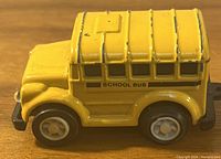 Side view of yellow metal school bus toy showing wheels, windows, and text 'SCHOOL BUS'