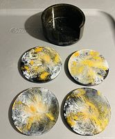 Photo of four round resin coasters with yellow, white, and black abstract patterns and a black holder with a notch