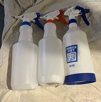 Photo of three plastic spray bottles side by side on fabric surface; one bottle has the Power Fist logo and 34 oz label.