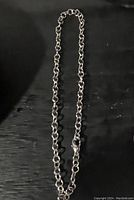 Photo of a silver tone chain link bracelet laid flat on a black surface, showing the full length and lobster clasp.