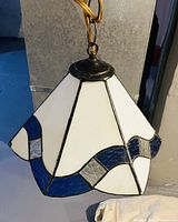 Photo showing the stained glass hanging lamp with white and blue glass panels, metal framing, and hanging chain.
