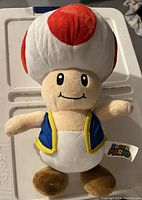Front view of a Super Mario Toad plush with red-spotted white mushroom cap and blue vest.