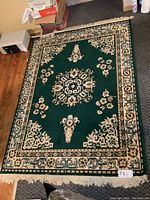 Full view of rectangular emerald green area rug with floral and geometric border designs and fringe on short edges