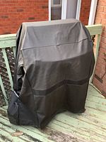 Propane BBQ grill covered with a black newer fitted protective cover showing pockets on front