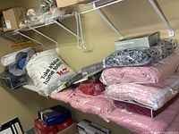 Wide view of bedding and blankets arranged on a shelf including pink bedding and packaged items.