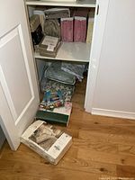 Closet lower shelves and floor with several packages of bedding sets and tablecloths in various colors and sealed packaging.