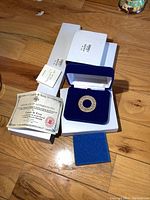 Overview showing circular brooch in blue velvet box, certificate and outer boxes