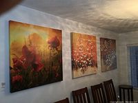 View of all three large canvas floral prints mounted on a wall above dining chairs.
