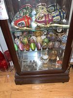 Wooden display cabinet showing top view of large porcelain hinged decorative eggs with ribbon ties on glass shelf