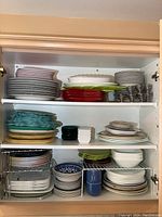 Full view of cupboard showing multiple shelves with stacks of dishes of various colors and patterns