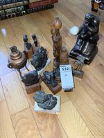 Overview of all figurines totaling approximately 12 items: metal, wood, and plaster, sizes up to 10 inches tall, arranged on hardwood floor.