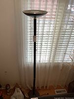 Full view of black torchiere floor lamp standing near window with sheer curtain backdrop.