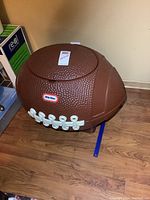 Side view of brown football shaped toy box with white laces and Little Tikes logo showing texture and shape.