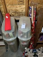 Two translucent Rubbermaid Wrap 'n Craft totes filled with rolled wrapping paper and a red handle on one tote lid