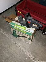 Electric hedge trimmer positioned on top of the Weed Eater leaf blower box showing the full length of the blade and handle.