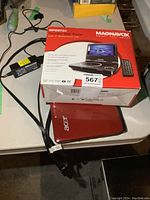 Magnavox MPD8710 portable DVD player box with description and red Acer laptop seen beneath the box, cables nearby