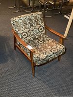 Front angle view of the MCM chair showing the patterned cushions and wooden frame with one armrest damage.