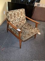 Photo showing front and side angle of vintage MCM solid wood chair with patterned cushioned seat and back resting on carpeted floor.