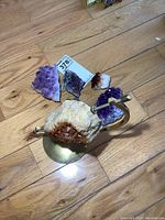 View of all precious stone pieces on wooden floor, showing three amethyst clusters and large citrine geode on brass stand.