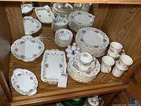 Full set of Royal Albert Tranquility dinnerware including plates, cups, saucers, mugs, and serving dishes visible in wooden cabinet.