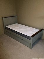 Assembled single bed frame with mattress and drawers in room.