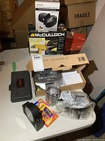 Various tools and electronic items including electric diamond knife sharpener, handheld steamer, battery charger, small tool kit, electrical tape, lighters, and clock arranged on a table.