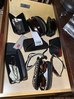 Top view of the lot showing various sunglasses and glasses with cases including Ray-Ban and leopard print cases.