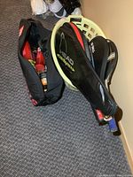 Three tennis rackets in HEAD covers and two tennis bags, basket holding rackets, bags sitting on floor