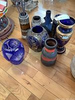 Overview of all eight vases on wooden floor, showing variety of materials and colors.