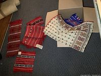 First photo showing several folded vintage fabric linens including red striped pieces and a white embroidered piece inside a box.