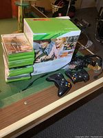 Overall lot photo with Xbox 360 console box, 16 Xbox 360 game cases stacked, 3 black controllers, headset, and various cables laid out on a pool table.
