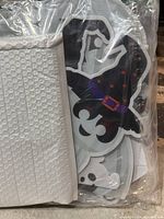 Photo of packaged 2D Halloween decoration showing ghost with witch hat and 'BOO' text, along with white textured backing.
