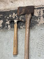 Photo of a worn, rusted axe and a smaller claw hammer lying on a concrete surface.